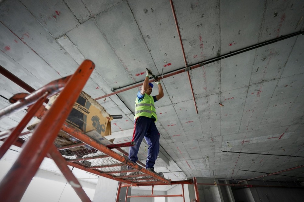 A maintenance worker fitting pipes on a building ceiling